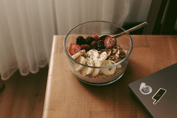 Glass bowl of oats with bananas, strawberries, and nuts on a wooden desk.