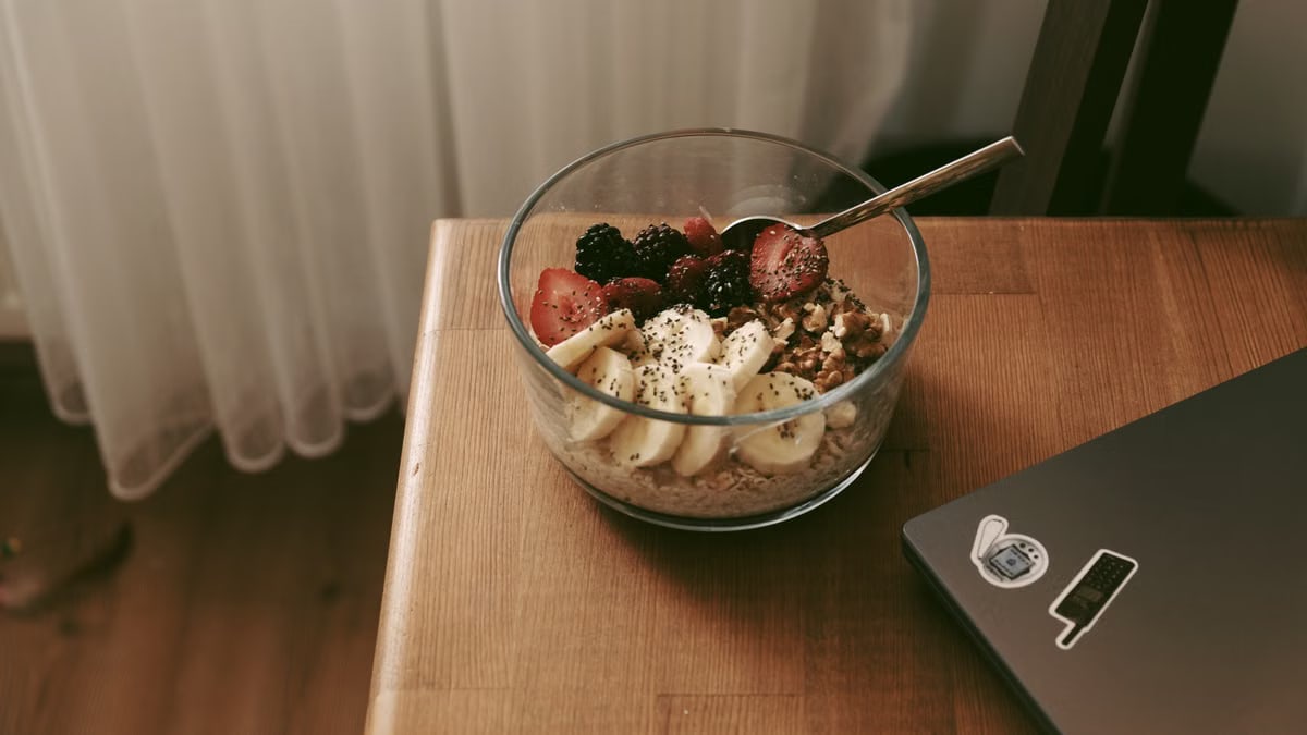 Glass bowl of oats with bananas, strawberries, and nuts on a wooden desk.