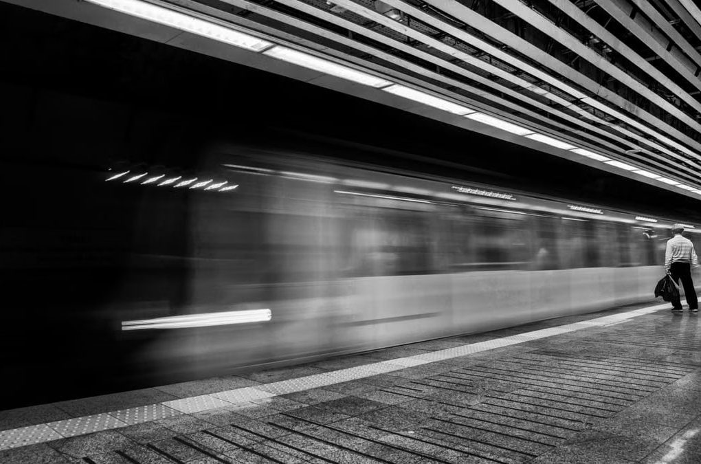 Motion blur of a speeding subway train with a solitary passenger on the platform.