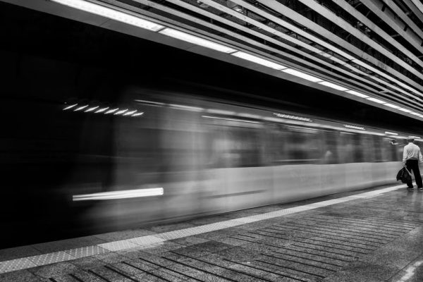 Motion blur of a speeding subway train with a solitary passenger on the platform.